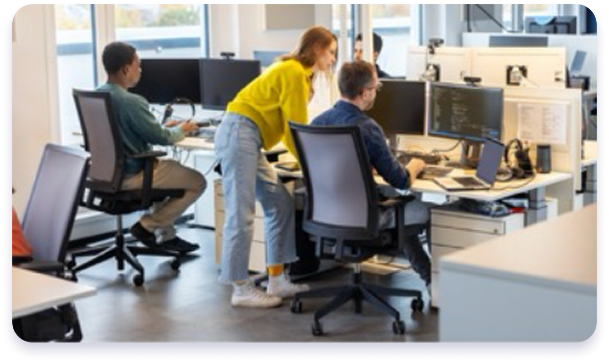 Team of developers collaborating at computer workstations in a modern office, reviewing code and digital projects together.