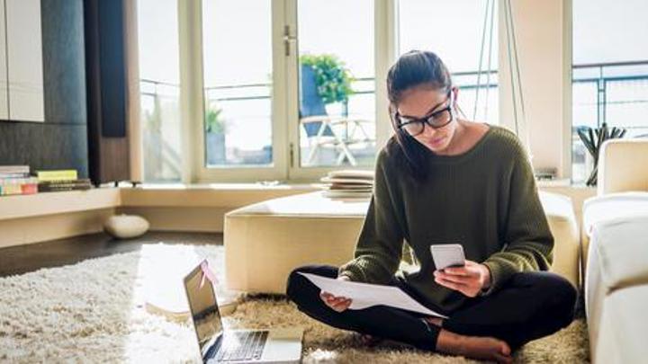 Person sititng down looking at their phone holding a piece of paper.