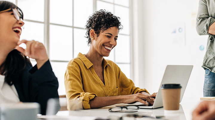 Group of people in a meeting laughing and collaborating on a laptop.